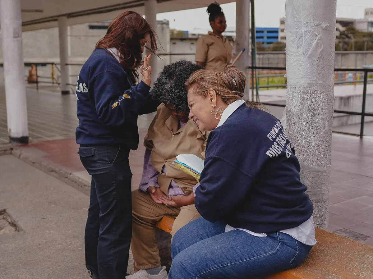 Dos mujeres de la fundación acompañan en oración a una mujer en el patio.